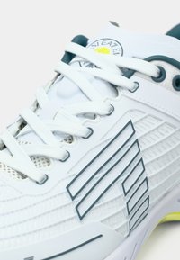 Fehér sportcipő, texturált felsőrésszel, hálós betétekkel, kék díszítésekkel és vastag átlós csíkokkal. Cipőfűző standard elrendezésben.