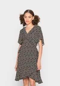 Vestido preto com decote em V, mangas esvoaçantes e bainha assimétrica. Apresenta um pequeno padrão de corações brancos e beges por todo o vestido.