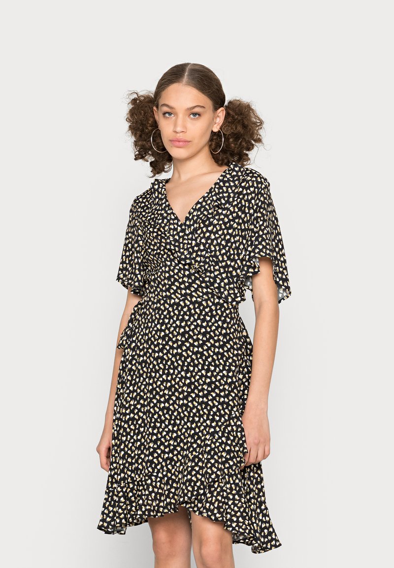 Vestido preto com decote em V, mangas esvoaçantes e bainha assimétrica. Apresenta um pequeno padrão de corações brancos e beges por todo o vestido.