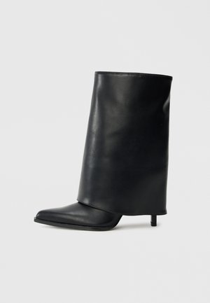 Bottine en cuir noir avec un design structuré à rabat, bout pointu et talon fin. Texture lisse avec un minimum de détails.