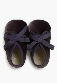 Dunkelvelourschuhe mit runder Spitze, ausgestattet mit breiten, dunkelblauen Bändern und einem weichen Innenfutter. Der Markenname ist in Gold geprägt.