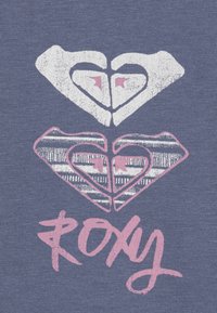 Tela azul con un gráfico impreso que presenta dos corazones superpuestos, uno en blanco con acentos en rosa y el otro con un patrón a rayas. Abajo, la palabra "ROXY" en cursiva rosa.