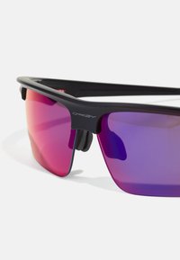 Ochelari de soare sport negri cu lentile gradient violet. Au un design elegant, formă înfășurată și accente din cauciuc pentru aderență.