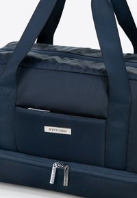 Navyblauwe sporttas van textuurstof, met dubbele handgrepen en een ritsvak. Voorzien van zilverkleurige hardware en een merkembleem.