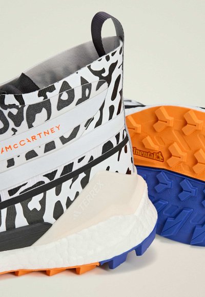 Vysoké športové topánky s bielym základom a čiernym leopardím vzorom, hrubou štruktúrovanou podrážkou v oranžovej a modrej farbe a s poutkom na zadnej strane.