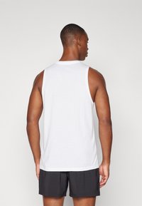 Débardeur blanc sans manches en coton, avec un col rond, une coupe décontractée et un ourlet droit. Porté avec un short noir.