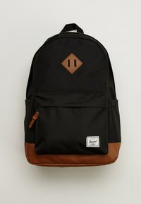 Black backpack made of durable fabric with a brown leather bottom. Features a diamond-shaped accent and front zip pocket. Classic design.