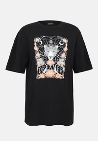Svart bomullst-skjorte med en hvit og ferskenfarget grafikk av en leopard omgitt av blomster og ordet "DREAMER." Oversized design.