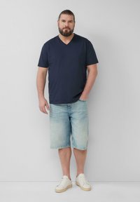 Marineblauw v-hals t-shirt gecombineerd met lichtblauwe spijker shorts, met een relaxte pasvorm. Witte sneakers maken de casual look compleet.