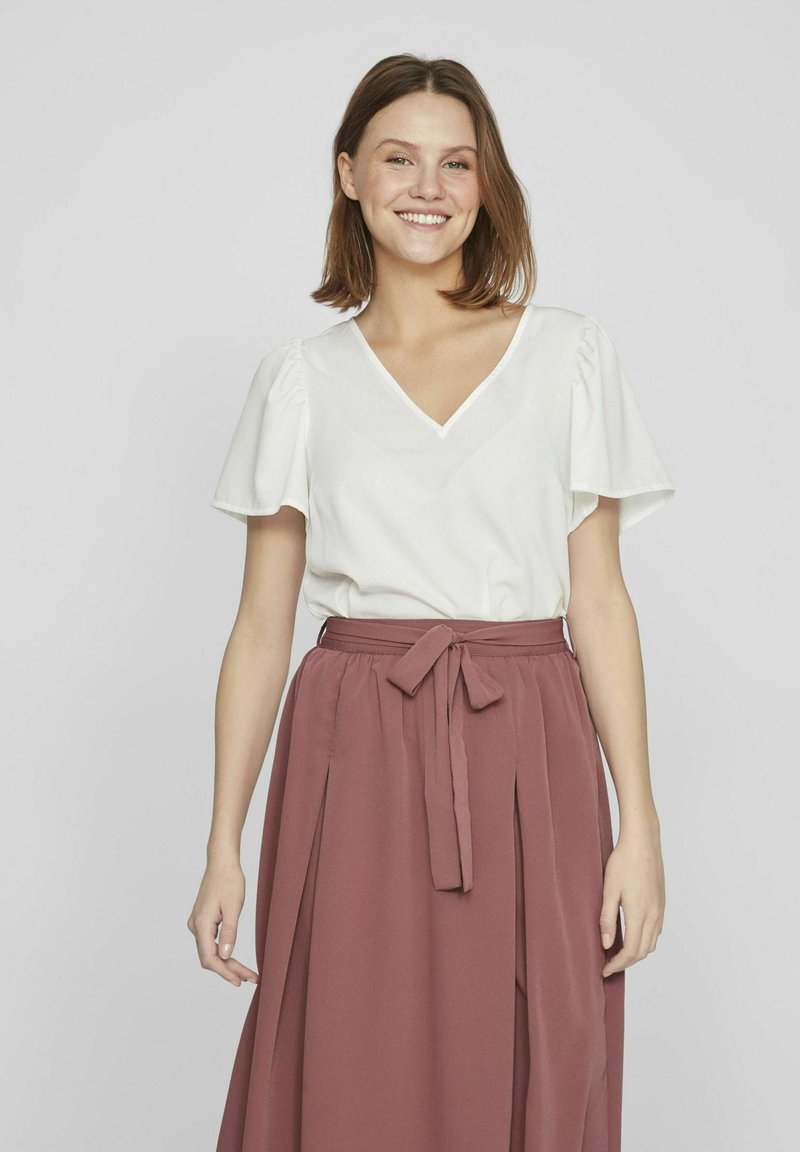 Witte V-hals top met korte puffmouwen, gecombineerd met een lange, vloeiende, rozenkleurige rok met een strik taille en plooidetail.