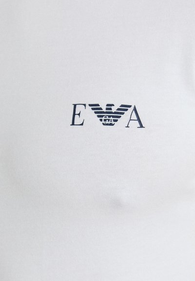 Fehér pamut póló, amely egy sötétkék logót tartalmaz vízszintes csíkokkal és az "EVA" felirattal a "GA" felett, a póló felső középső részén elhelyezve.