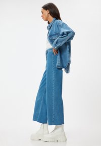 Chaqueta de mezclilla azul clara y pantalones de pierna ancha, combinados con botas blancas gruesas y con cordones. Textura suave, corte relajado y detalles de costura visibles.