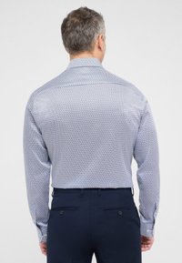 Langærmet skjorte med et geometrisk mønster i blå og hvid. Klassisk krave og knapmanchetter. Sammen med marineblå bukser.