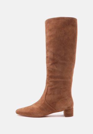 Botte haute en daim marron avec un petit talon bloc et un bout pointu sur un fond clair uni.