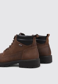 Botas de cuero marrón con un cuello acolchado negro, diseño de cordones, suela de goma y detalles de costura en contraste.