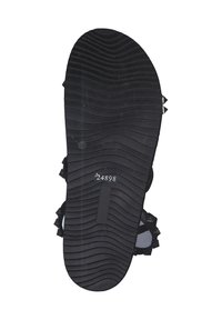 Black rubber shoe sole featuring a textured, wavy pattern with grooves, multiple grip studs, and a printed code for identification.