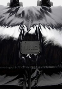 Borsa tote nera lucida con superficie texturizzata, con un'etichetta loggata rettangolare etichettata "LIU•JO" in uno stile a contrasto.