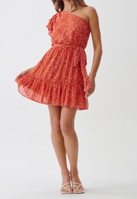 Robe à motif floral rouge avec une épaule, détail à volants, taille ceinturée et ourlet à volants superposés. Tissu léger et fluide.