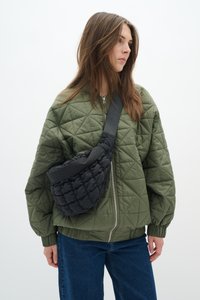Veste bomber olive matelassée avec des poignets côtelés, associée à un sac bandoulière noir rembourré avec une sangle lisse et une forme arrondie.