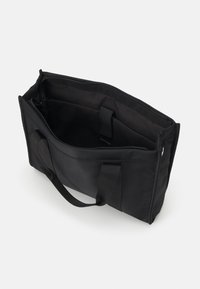 Sac fourre-tout en tissu noir de forme rectangulaire, avec fermeture éclair et double poignée. Le compartiment intérieur présente une texture douce sans motifs visibles.