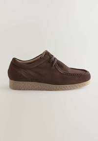 Brune ruskindsko med et syet design, rund tå og en struktureret beige gummisål. Har grå snørebånd og en lavprofilform.