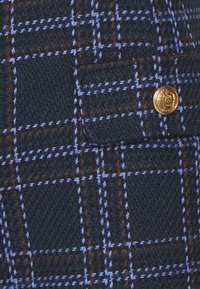 Navy blue textured fabric with a plaid pattern, featuring thin blue and brown lines. Includes a gold button detail on a pocket.