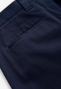 Marineblauwe broek met een gladde textuur, voorzien van een achterzak en riemlussen. De stof heeft een fijne ribbelpatroon.