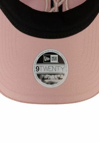 Rosa Kappe mit schwarzem Schirm, mit einem runden Etikett, das "NEW ERA 9TWENTY WOMEN" und "VERSTELLBAR" angibt. Strukturiertes Material.