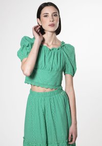 Completo due pezzi verde con top cropped a maniche puff e orlo scallop, abbinato a una gonna coordinata con vita arricciata.