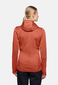 Maglia con cappuccio a maniche lunghe di colore arancio ruggine, con un motivo testurizzato e un design aderente. Caratterizzata da aperture per il pollice nei polsini e una cucitura posteriore per una migliore vestibilità.