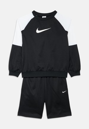 Set format din bluză sport cu mânecă lungă Nike alb-negru și pantaloni scurți negri, cu logo-uri albe Nike Swoosh pe piept și pe pantaloni scurți.