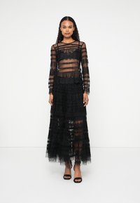 Black lace dress with long sleeves, sheer layers, ruffled hem, and fitted bodice. Features horizontal stripes and a flowy silhouette.