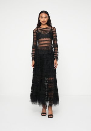 Vestido negro de encaje con mangas largas, capas transparentes, dobladillo con volantes y cuerpo ajustado. Presenta rayas horizontales y una silueta fluida.