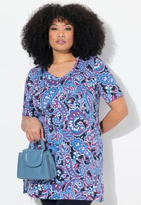 Tunique à manches courtes arborant un motif paisley vibrant en rouge, bleu et blanc sur un fond sombre. Accompagnée d'un petit sac à main bleu.