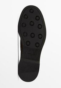 Black shoe sole with circular traction dots, smooth texture, and a slight curved shape. Features a brand imprint along the side.