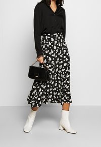 Blusa negra de botones con mangas largas, combinada con una falda midi de patrón floral en blanco y negro. Botines blancos y un pequeño bolso negro.
