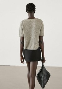 Top a maniche corte in maglia testurizzata beige con una vestibilità ampia, abbinato a una mini gonna nera aderente e a una borsa intrecciata nera.