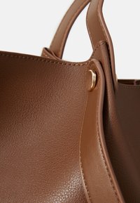 Borsa a tracolla in pelle marrone con superficie testurizzata, dotata di manici lisci e dettagli in metallo dorato. La forma è leggermente strutturata con bordi arrotondati.