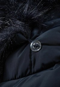 Chaqueta de plumas negra con un acabado brillante, que presenta un cuello elevado adornado con un suave y largo pelo sintético negro y un cierre de botón transparente.