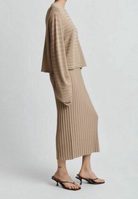 Beige žebrovaný pletený top s širokými rukávy, spárovaný s odpovídající midi sukní ze žebrovaného materiálu. Nosené s černými sandály na podpatku se šňůrkami. Hladká textura.