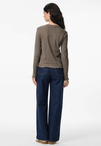 Top a maniche lunghe marrone a costine con orlo a scallop, abbinato a jeans a vita alta e gamba larga blu scuro e scarpe beige.