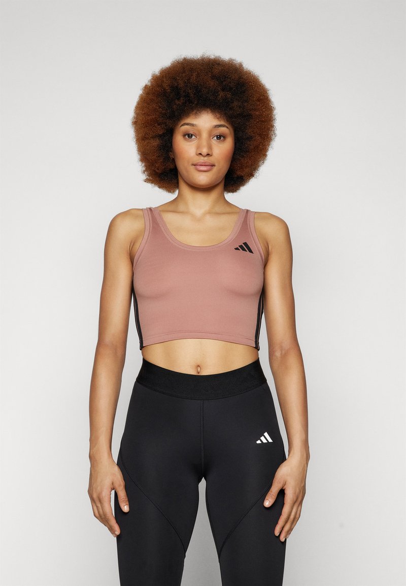 Crop topp i støvete rosa med svarte sidestykker, med scoop-hals og svart logo. Kombinert med høy midje svarte leggings.
