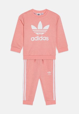Tuta in cotone rosa con top a girocollo decorato dal logo Adidas bianco e tre strisce bianche sui pantaloni. Include polsini e vita a coste.