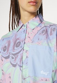 Kurzarm-Hemd mit Knopfleiste in einem pastellfarbenen abstrakten Muster, blauer Tasche und blauen Knöpfen, aus einem strukturierten Baumwoll-Mischgewebe gefertigt.