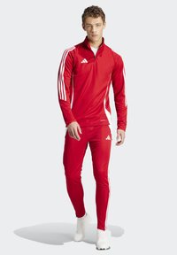 Red athletic tracksuit with a half-zip top and slim-fit pants. Features white stripes along sleeves and sides. Made of smooth, stretchy fabric.