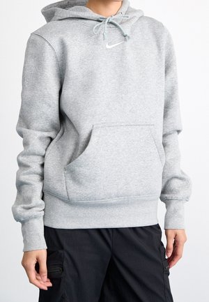 Person iført en lysegrå Nike hættetrøje med frontlomme og snørrehætte kombineret med sorte cargobukser.