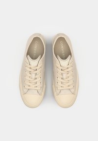 Zapatillas de lona beige con parte superior texturizada, puntera redonda y cordones en el mismo tono. Presentan el logo en relieve "CONVERSE" en la plantilla. Diseño de suela plana.