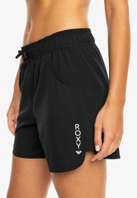 Svarte shorts med elastisk midjebånd, snor, sidelommer og "ROXY"-logo trykt i hvitt på siden. Myk, stretchy stoff.