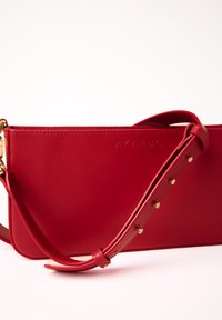 Borsa a tracolla in pelle rossa con texture liscia, tracolla regolabile con borchie dorate e logo impresso. Forma rettangolare slim.