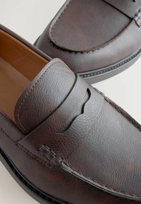 Brązowe skórzane loafersy z detalicznym przeszyciem, płaskimi podeszwami, teksturowanym wykończeniem oraz falistym wzorem na górnej części.